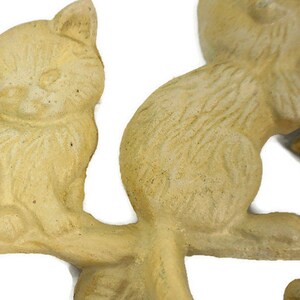 Puede incluir: Un conjunto de cuatro ganchos de cer&aacute;mica de color crema en forma de gato, cada uno en una pose diferente, montado en una rama. Los ganchos est&aacute;n dise&ntilde;ados para sujetar llaves, bufandas u otros objetos peque&ntilde;os.