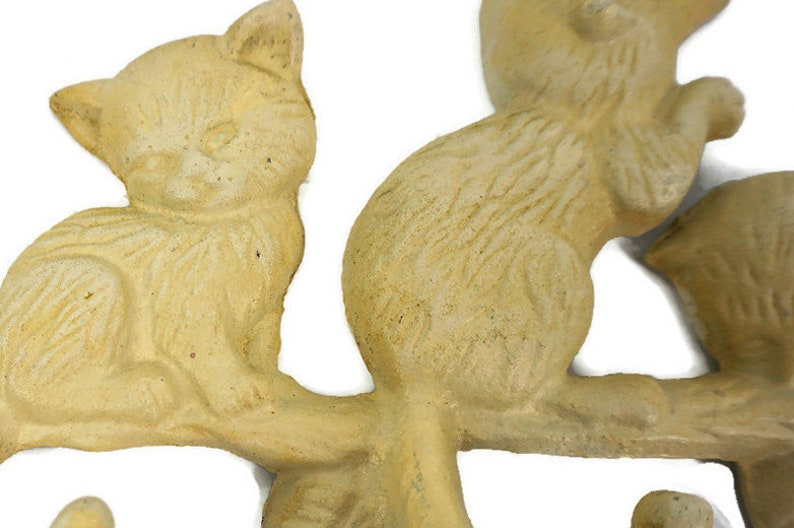 Puede incluir: Un conjunto de cuatro ganchos de cer&aacute;mica de color crema en forma de gato, cada uno en una pose diferente, montado en una rama. Los ganchos est&aacute;n dise&ntilde;ados para sujetar llaves, bufandas u otros objetos peque&ntilde;os.
