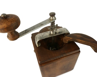 May include: A vintage wooden coffee grinder with a metal crank and a wooden handle. The grinder has a dark brown finish and a rectangular shape.