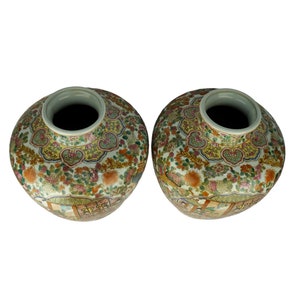 May include: Two white ceramic vases with intricate floral and geometric patterns in shades of blue, green, yellow, and red. The vases have a round body and a wide opening at the top.