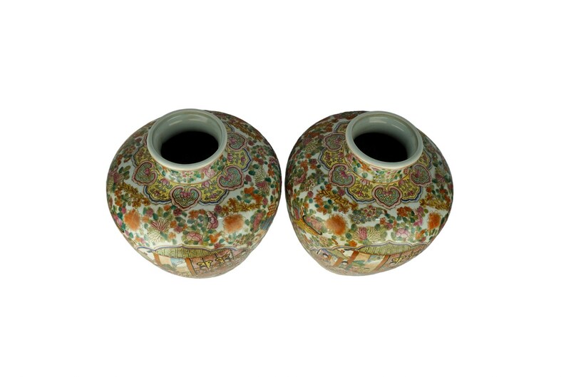 May include: Two white ceramic vases with intricate floral and geometric patterns in shades of blue, green, yellow, and red. The vases have a round body and a wide opening at the top.