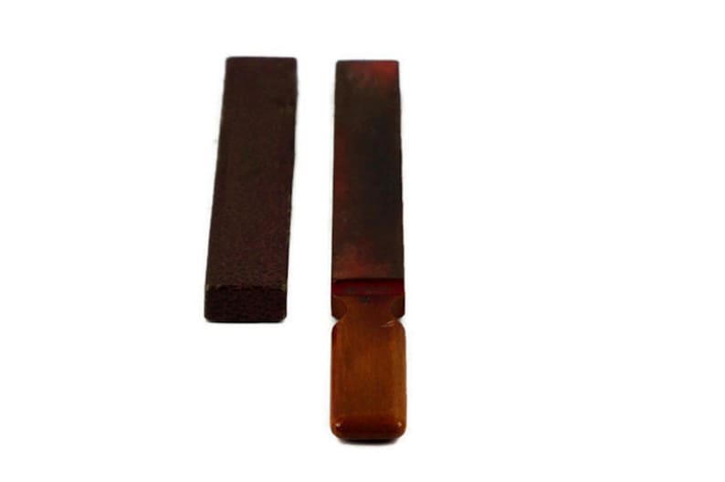 May include: Two sharpening stones, one with a wooden handle and one without. Both stones are brown and red.