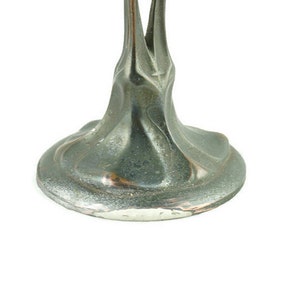 May include: A silver metal base with a swirling, organic design. The base is smooth and has a slight sheen.