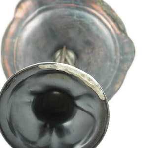 May include: A silver-toned metal candlestick with a round base and a decorative top. The base has a dark patina and the top has a lighter patina.