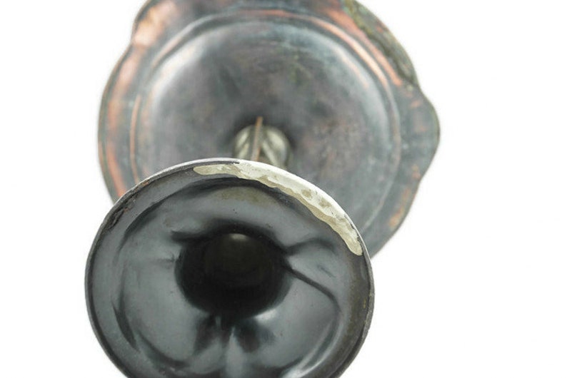 May include: A silver-toned metal candlestick with a round base and a decorative top. The base has a dark patina and the top has a lighter patina.