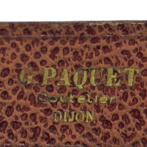 May include: Close-up of a brown leather box with gold lettering that reads "G. Paquet Couteller Dijon".