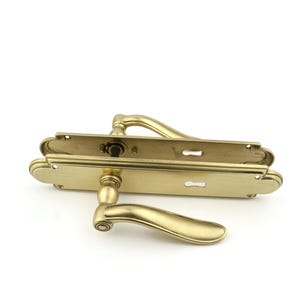 Peut inclure: Une poignée de porte dorée avec un levier incurvé et une plaque arrière rectangulaire. La poignée est de style traditionnel.