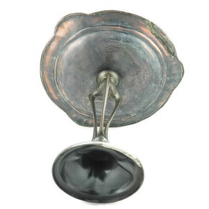 May include: A silver-plated pedestal with a round, scalloped top. The top is made of a dark metal with a copper-colored patina. The pedestal is designed to hold a small object, such as a dish or a bowl.