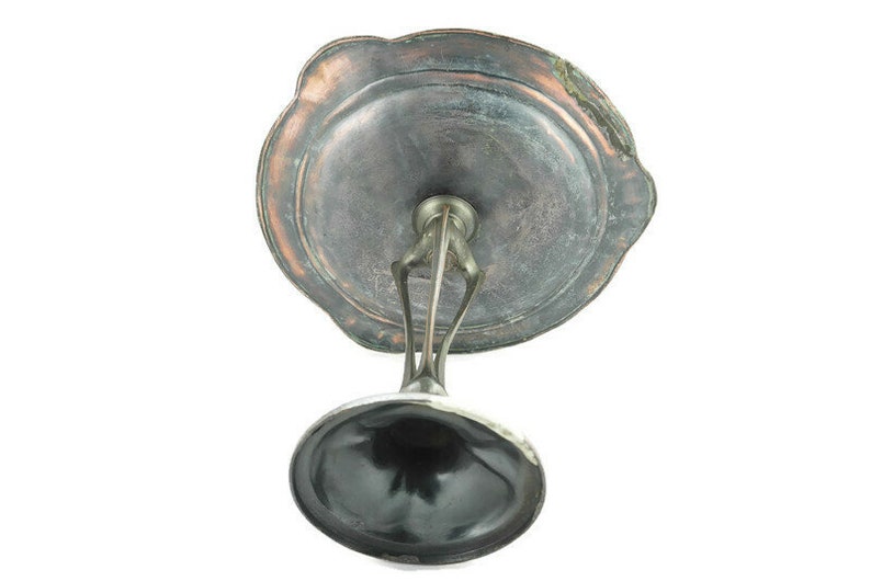 May include: A silver-plated pedestal with a round, scalloped top. The top is made of a dark metal with a copper-colored patina. The pedestal is designed to hold a small object, such as a dish or a bowl.