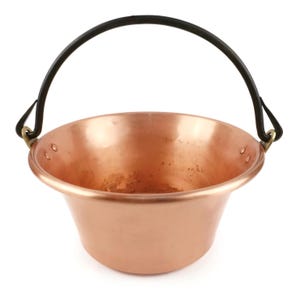 Puede incluir: Una olla de cobre pulido con un borde ancho y acampanado y una base redondeada. La olla cuenta con un asa de metal oscuro y curvada, sujeta a los lados con herrajes de color latón. La superficie interior muestra un acabado metálico texturizado.