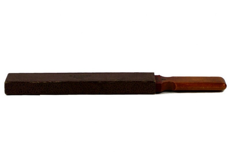 May include: A brown leather case with a wooden handle. The case is closed and appears to be for a small tool or instrument.
