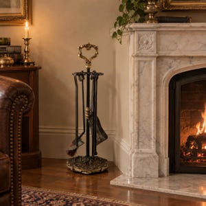 Puede incluir: Un juego de herramientas para chimenea de metal negro con mango y base ornamentados en tonos dorados. El conjunto incluye una pala, un atizador y un cepillo, suspendidos de un soporte central con un remate decorativo en forma de corazón.
