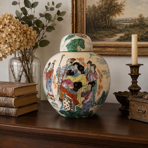 Può includere: Un barattolo per zenzero in ceramica color crema con coperchio abbinato, caratterizzato da una dettagliata scena dipinta a mano con diverse figure in abiti tradizionali. Il barattolo mostra colori vivaci tra cui rosso, giallo, blu e verde.