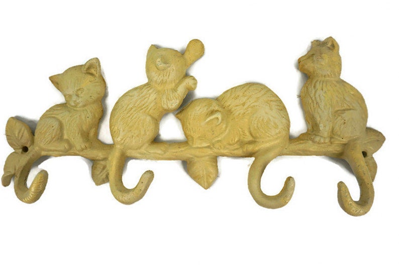Puede incluir: Un colgador de llaves de hierro fundido amarillo con forma de rama con cuatro gatos. Dos gatos est&aacute;n sentados en la rama, uno est&aacute; durmiendo en la rama y uno est&aacute; colgado de la rama. La rama tiene tres ganchos para colgar llaves.