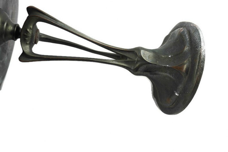 May include: A silver-toned metal base with an intricate design. The base has a wide, flat top and three curved legs that extend out from the center. The legs are decorated with a floral pattern.