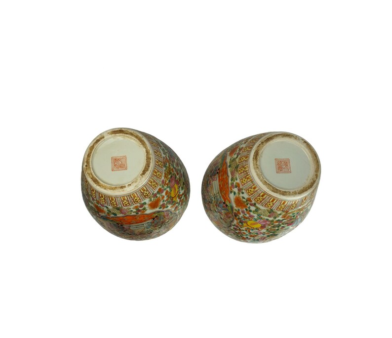 May include: Two white ceramic vases with a floral pattern in shades of orange, yellow, and green. The vases have a gold trim and a red seal on the bottom.