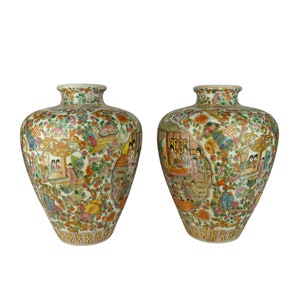 May include: Two white porcelain vases with a floral and figural design. The vases are decorated with a colorful pattern of flowers, birds, and people. The vases are approximately 12 inches tall.