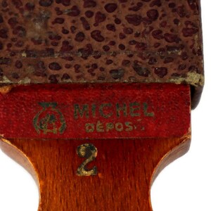 May include: A wooden razor strop with a red leather top and a brown leather backing. The strop has the text "MICHEL DEPOS." and the number "2" printed on it.