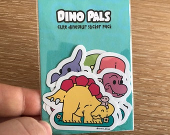 May include: A sticker pack with four cute dinosaur stickers. The stickers are on a blue background with the text "Dino Pals cute dinosaur sticker pack".