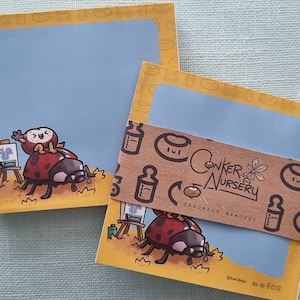 May include: Two packs of yellow and blue notepad paper with a ladybug and a small bird illustration. The notepad paper is labeled "Conker Nursery Handmade Memorabilia".