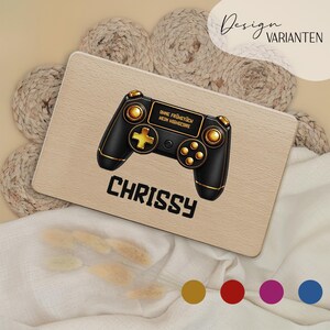 Könnte beinhalten: Ein rechteckiges Holzbrett mit einer Grafik eines schwarz-goldenen Gamecontrollers, dem Text "OHNE FRÜHSTÜCK KEIN HIGHSCORE" und dem Namen "CHRISSY" in Schwarz. Das Brett hat eine helle Holzmaserung und abgerundete Ecken.