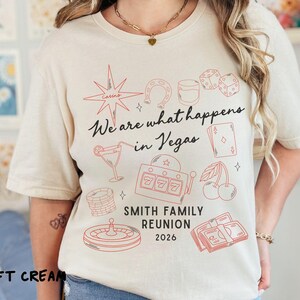 May include: Soft cream-colored t-shirt with a red graphic design featuring casino-themed illustrations and the text "We are what happens in Vegas." Includes the text "SMITH FAMILY REUNION 2026."