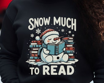 May include: Black sweatshirt with a snowman wearing a Santa hat reading a book. The text on the sweatshirt says "Snow Much To Read".
