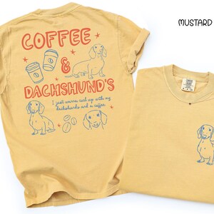 May include: Mustard-colored t-shirts with dachshund and coffee-themed graphics. One shirt features a large design on the back with text and illustrations, while the other has a small dachshund graphic on the front pocket.