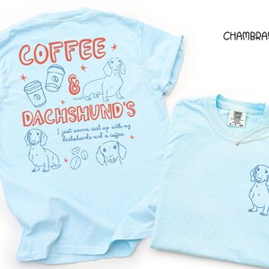 May include: Two light blue t-shirts. One has a dachshund graphic on the front and the text "Coffee & Dachshund's" with coffee cups and dachshund illustrations on the back. The other shirt has a dachshund graphic on the front.