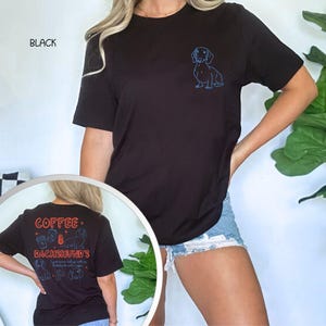 May include: Black t-shirt with a blue dachshund graphic on the front and the word "BLACK" at the top left. The back of the shirt features the text "COFFEE & DACHSHUND'S" with coffee cup and dachshund illustrations in red and blue.