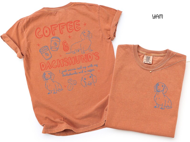 May include: Two orange-colored t-shirts. One shirt has the text "Coffee & Dachshund's" with illustrations of coffee cups and a dachshund. The other shirt has a small dachshund illustration on the front. The shirts are made of a soft material.
