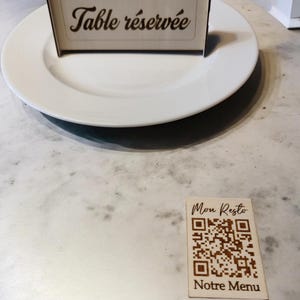 Peut inclure: Une pancarte en bois avec le texte "Table réservée" sur une assiette blanche. Une deuxième pancarte en bois avec le texte "Mon Resto" et un code QR avec le texte "Notre Menu" en dessous.