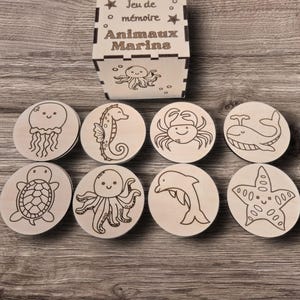 Peut inclure: Jeu de mémoire en bois avec des illustrations d'animaux marins. L'ensemble comprend huit tuiles rondes en bois avec des gravures d'une méduse, d'un hippocampe, d'un crabe, d'une baleine, d'une tortue, d'une pieuvre, d'un dauphin et d'une étoile de mer.