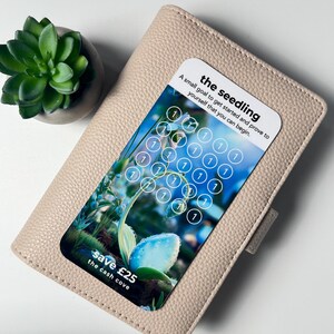 Puede incluir: Una cartera de cuero beige claro con una tarjeta que presenta un dise&ntilde;o floral y el texto "the seedling". La tarjeta tiene una cuadr&iacute;cula de c&iacute;rculos con el n&uacute;mero "1" en su interior. Se ve una peque&ntilde;a planta suculenta en una maceta gris.