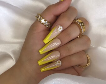 May include: Long, yellow and nude press-on nails with white flower accents.