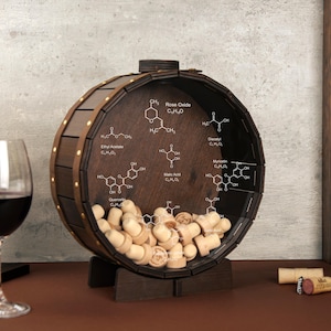 May include: A wooden barrel-shaped wine cork holder with a clear glass front. The holder is filled with cork stoppers and has the chemical formulas for various wine compounds printed on the wood.
