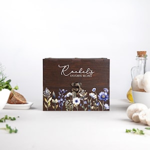 May include: A wooden recipe box with a floral design and the text "Rachel's Favorite Recipes" on the lid.