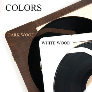 May include: A wooden record player with a black vinyl record. The player is available in two colors: dark wood and white wood. The text "COLORS" is displayed at the top of the image. The text "DARK WOOD" is displayed on the dark wood side of the player. The text "WHITE WOOD" is displayed on the white wood side of the player.