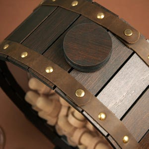 May include: A wooden wine bottle holder shaped like a barrel with a brown leather strap and brass accents. The barrel is made of dark wood and has a circular cutout in the top.