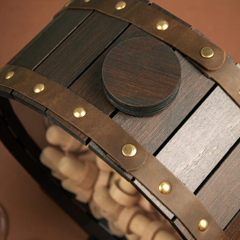 May include: A wooden wine bottle holder shaped like a barrel with a brown leather strap and brass accents. The barrel is made of dark wood and has a circular cutout in the top.