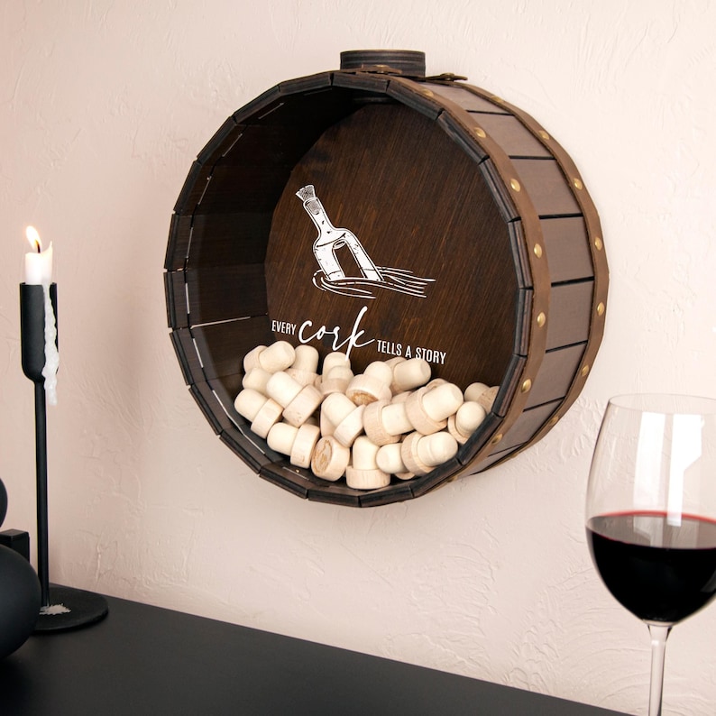 May include: A brown wooden barrel-shaped wall mounted cork holder with a white inscription that reads "Every cork tells a story". The holder is filled with cork bottle stoppers.