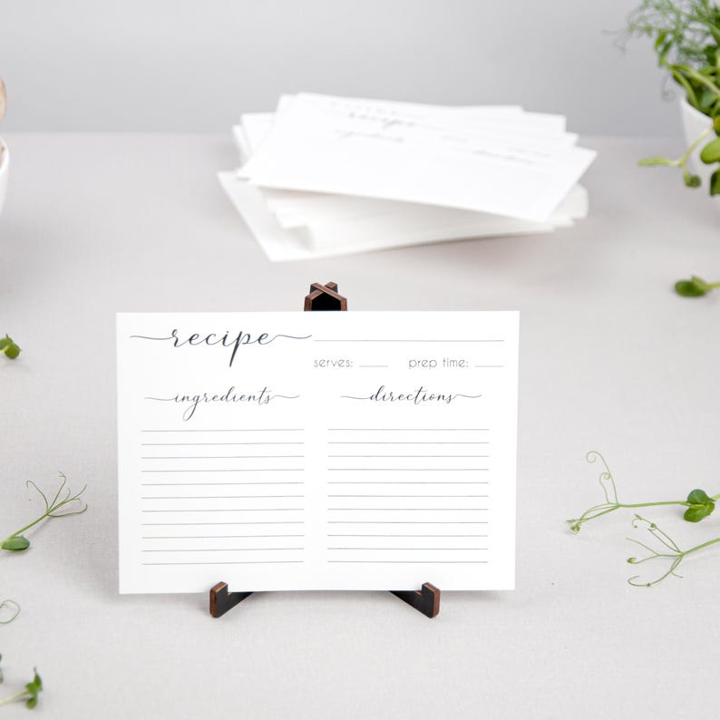 May include: A blank recipe card with lines for ingredients and directions. The card is white with black text and is standing on a wooden easel.