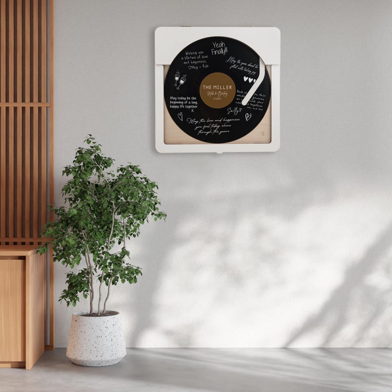 May include: A white frame with a black vinyl record inside. The record has handwritten messages on it, including "The Miller" and "Yeah Finally". The frame is hanging on a white wall.
