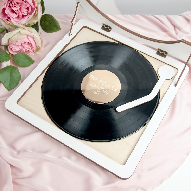 May include: White wooden record player with a black vinyl record inside. The record has a gold sticker with the text "The Miller Wedding" on it.