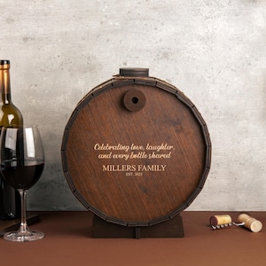 May include: A wooden barrel with a personalized inscription: "Celebrating love, laughter, and every bottle shared. Millers Family Est. 2025". The barrel is brown and has a wooden stand.