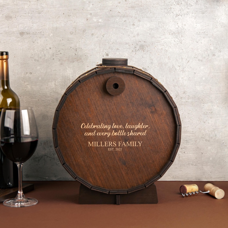 May include: A wooden barrel with a personalized inscription: "Celebrating love, laughter, and every bottle shared. Millers Family Est. 2025". The barrel is brown and has a wooden stand.