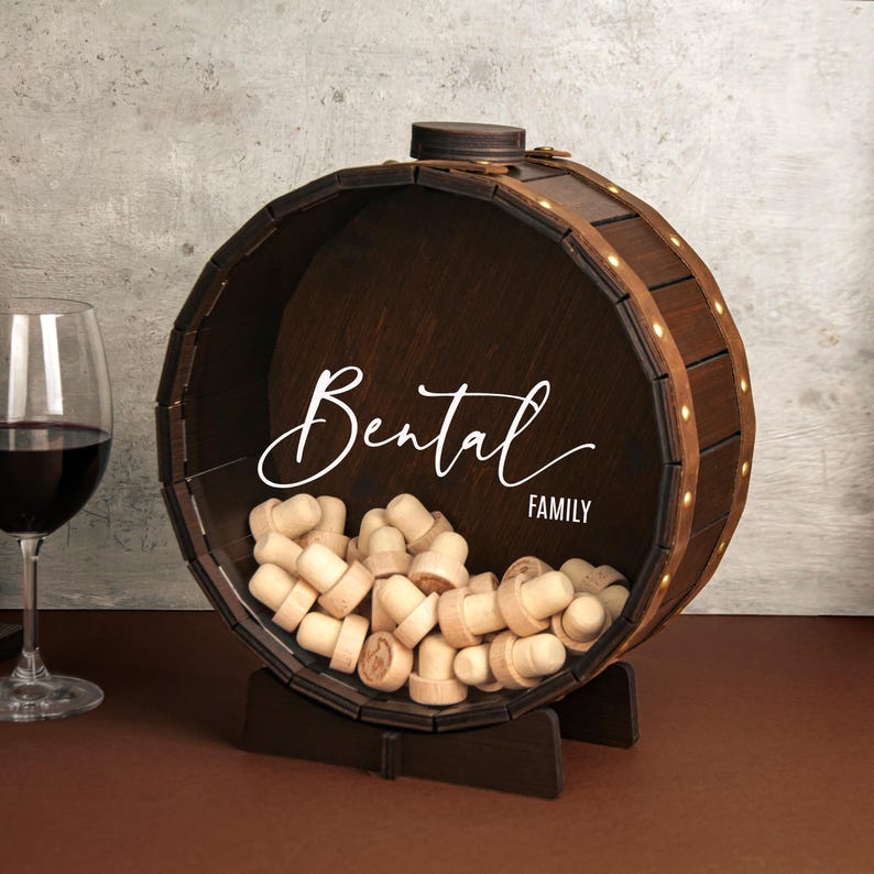 May include: A wooden wine cork holder shaped like a barrel with a stand. The barrel is brown and has a white inscription that reads "Bental Family". The barrel is filled with wine corks.