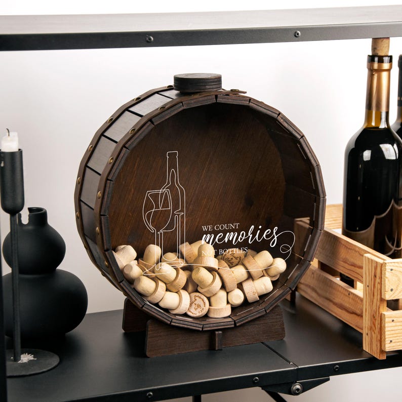 May include: A wooden barrel-shaped wine cork holder with a brown finish. The holder is filled with wine corks and has a sign that reads "We count memories not bottles".
