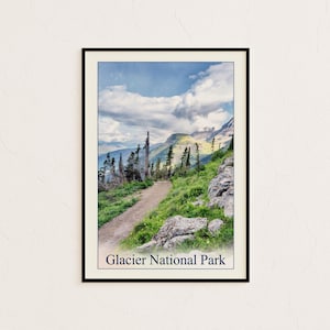 May include: A framed print featuring a scenic view of Glacier National Park. The image showcases a dirt path winding through a lush green hillside, with towering trees and rocky terrain. The sky is a mix of blue and white clouds. The text "Glacier National Park" is at the bottom.