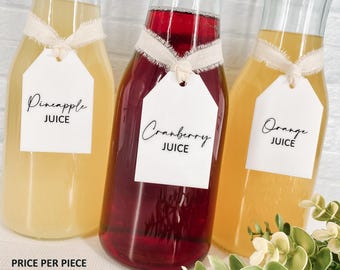 May include: Three glass juice bottles with white tags and cream-coloured ribbon. The bottles contain pineapple, cranberry, and orange juice. The tags read "Pineapple Juice", "Cranberry Juice", and "Orange Juice". The bottles are arranged in a row.